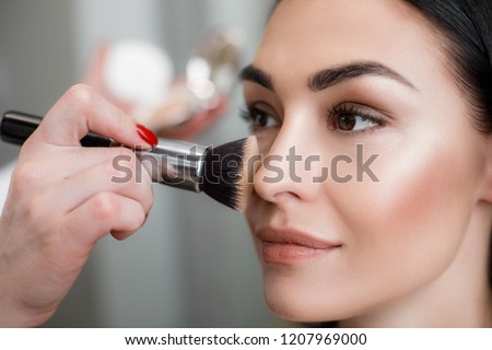 Close up of makeup artist applying light layer of matting powder while using professional brush for lady Royalty-Free Stock Photo #1207969000