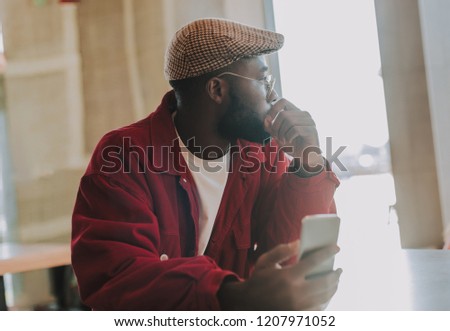 Thinking. Calm young man holding modern smartphone and thoughtfully looking into the distance