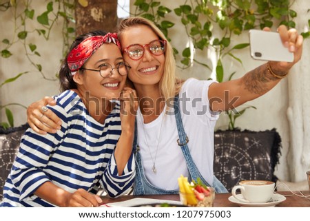 Best female friends have fun together, embrace and photograph herself for doing selfie, rest in cozy coffee shop, take pictures for publication on website. Technology and communication concept