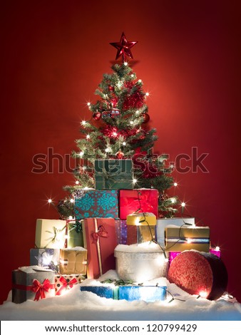 beautifully decorated christmas tree surrounded by a pile of colorful presents covered with snow on red background