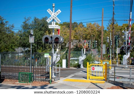 Open pedestrian railroad crossing gate with warning sign and crossing signal on the bright sunny day