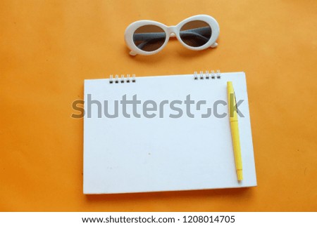  top view pen notbook, camera, glasses, on an orange background with space for text. flat lay