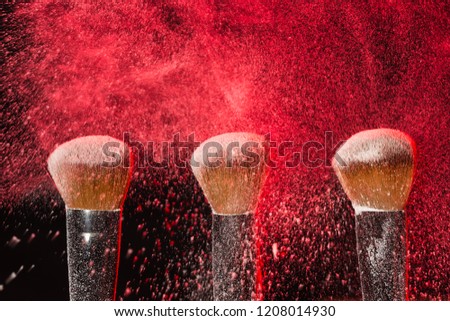 Make up, beauty, mineral cosmetic concept - powder brush on black background with red powder splashed on it