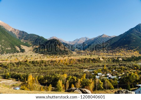 Colorful scene of mountains on a sunny day. Autumn landscape view of the valley with colorful trees and high peaks.
