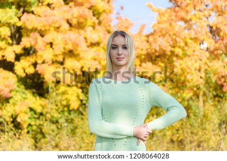 Photo portrait of a beautiful blonde girl in the park on the nature in the forest. She is standing right in front of the camera, smiling and looking happy.