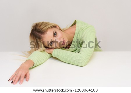 Photo portrait of a beautiful blonde girl talking on a white background sitting at the table. She is right in front of the camera, smiling and looking happy.