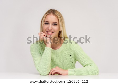 Photo portrait of a beautiful blonde girl talking on a white background sitting at the table. She is right in front of the camera, smiling and looking happy.