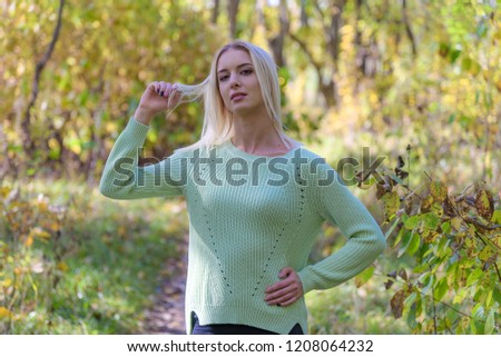 Photo portrait of a beautiful blonde girl in the park on the nature in the forest. She is standing right in front of the camera, smiling and looking happy.