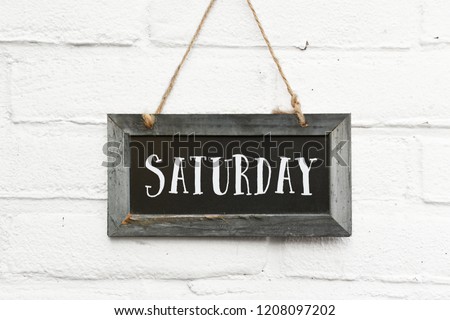 Hello saturday finally weekend text on hanging sign board against white brick outdoor wall Royalty-Free Stock Photo #1208097202