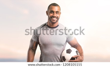 Strong football player with soccer ball and smiling on sunset background