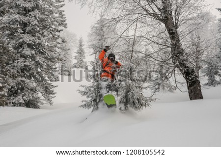 Male snowboarder jumping between trees on the powdered snow in the mountain tourist resort in Goderzi, Georgia
