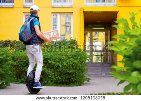 Modern future delivery. Man male guy in delivery uniform and delivery box with electric transport / eco ecology electric unicycle / self balancing wheel delivers ordered package to receiver Royalty-Free Stock Photo #1208106058