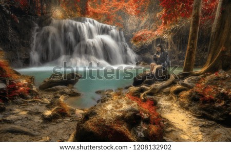 The backpack tourist woman sit on the rock in front of beautiful waterfall. she check the photo after took the shot