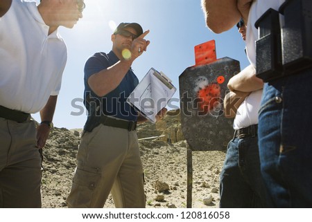 Instructor holding clipboard in front of group on shooting range Royalty-Free Stock Photo #120816058