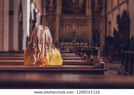 Young woman praying and meditating in church. Belief in Jesus Christ. Catholic cathedral with symbol of religion Royalty-Free Stock Photo #1208161126