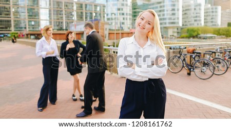 Blonde secretary looking at camera and playing with hair near talking employees background. Concept of businessperson and La Defense Paris. Young blonde woman is beautiful.