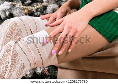 women's legs in white fishnet stockings and women's hands with pink manicure on Christmas tree background