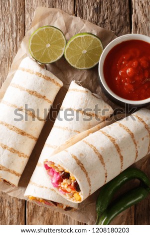 vegetarian burrito stuffed with rice and vegetables served with tomato sauce closeup on the table. Vertical top view from above

