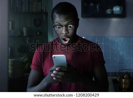 Close up portrait of african american man looking agitated at display of his smartphone with opened mouth, impressed by media content from web