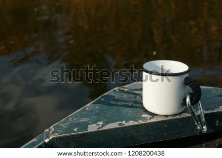 Camping mug on the boat in the autumn lake