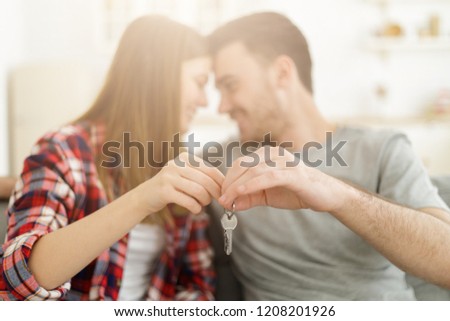 Young happy smiling couple holding set of keys, sitting on sofa face to face. New family concept