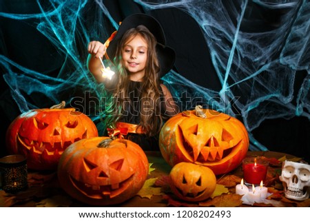 Halloween Witch concept - little witch child enjoy playing with magic wand over spider web and with curved pumpkins background.
