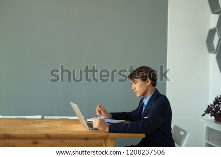 nice young guy businessman in suit sitting at table in office with laptop