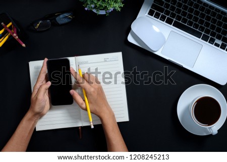 Woman hands holding a smart phone on work desk.Top view,Flat lay.