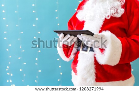 Santa holding a tablet computer on a shiny light blue background