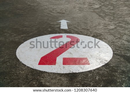 Red number two inside a white circle and an arrow painted on concrete background - 45 degrees angle view