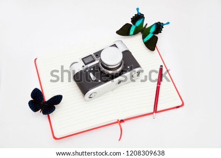 Two blue morpho butterfly and a camera lie on an open notebook and a ballpoint pen lies next to it. Explore butterflies, ethnology