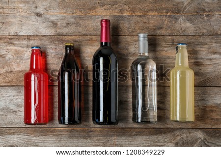 Bottles with different alcoholic drinks on wooden background, top view
