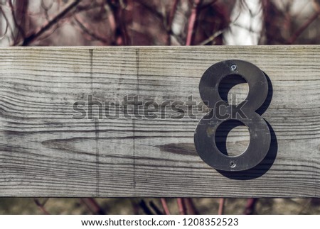 Metal number eight fixed with screws on wooden plank. Sign 8 on wooden unpainted surface under the bright sun. The sun makes shadows in shape of the number. Place space for your own text. Sunny day.