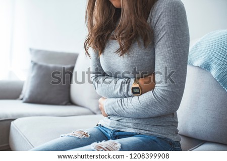 Woman lying on sofa looking sick in the living room. Beautiful young woman lying on bed and holding hands on her stomach. Woman having painful stomachache on bed, Menstrual period Royalty-Free Stock Photo #1208399908