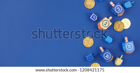 Dark blue background with multicolor dreidels and chocolate coins on the right. Hanukkah and judaic holiday concept. Horizontal, wide screen banner format