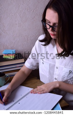 Young woman wearing glasses is going to write in a notebook at desk