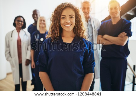 Smiling young female doctor standing in a hospital corridor with a diverse group of medical staff standing behind her Royalty-Free Stock Photo #1208448841