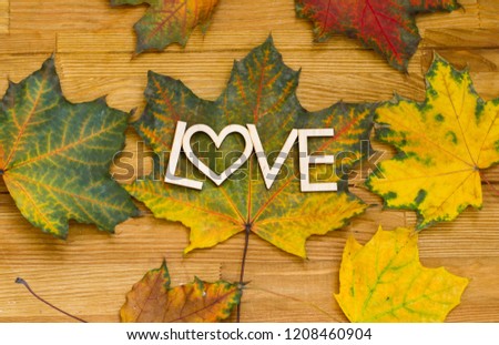 Wooden inscription LOVE on an autumn leaf on a wooden rural table. Shot from above.
