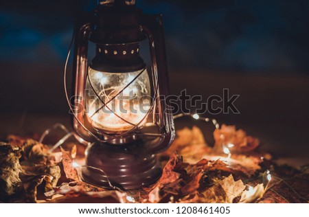 Vintage kerosene oil lantern lamp burning with a soft glow light in an antique rustic wood table with autumn leaves