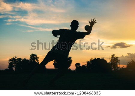 An action sport picture of a group of kid playing soccer football for exercise in community rural area under the twilight sunset sky. Silhouette picture from behind the goal keeper view .
