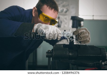 Man worker is working with iron detail on vise grip on blacksmith table and is measuring a diameter of machine part by caliper.