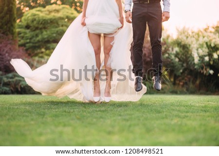stopped moment, a leap, jump in the air as if the bride and groom are flying above the green grass in the garden, no faces on the picture, the girl’s bare legs, art processing photo