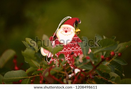 Wooden christmas decoration Santa Claus sitting on green branch with red berries. Merry Christmas and New Year concept 