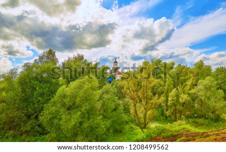 Vibrant view of country side near Vladimir, Russia, with an orthodox church with golden cupola surrounded by green trees under summer cloudy sky 