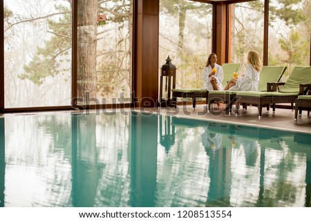 Two pretty young women relaxing on the deckchair by the swimming pool in spa Royalty-Free Stock Photo #1208513554