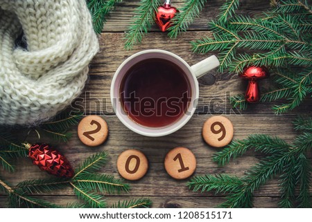 Tinted Christmas picture with 2019 new year on cookies, fir branches, toys, warm scarf and a mug of hot tea on a wooden background
