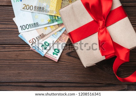 Wooden background, money of different value, and a precious gift. Top view.