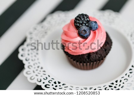 Chocolate cupcake with pink cream and berries served on white lace decorated plate on striped  black and white table