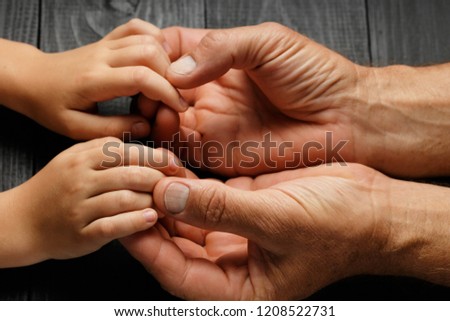 Top view, Adult hands holding kid hands, Family Help Care Concept, small hands in fathers hand. on black wooden background