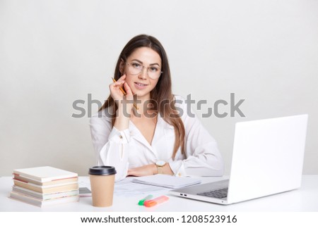 Photo of pretty Caucasian woman with long hair, wears spectacles, watches webinar on laptop computer, prepares project, does homework, drinks takeawway coffee, isolated over white background